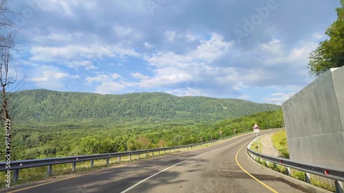 Driving a car on an asphalt mountain road in the forest and mountains in summer. Sunny day with blue sky and white clouds in summer.
