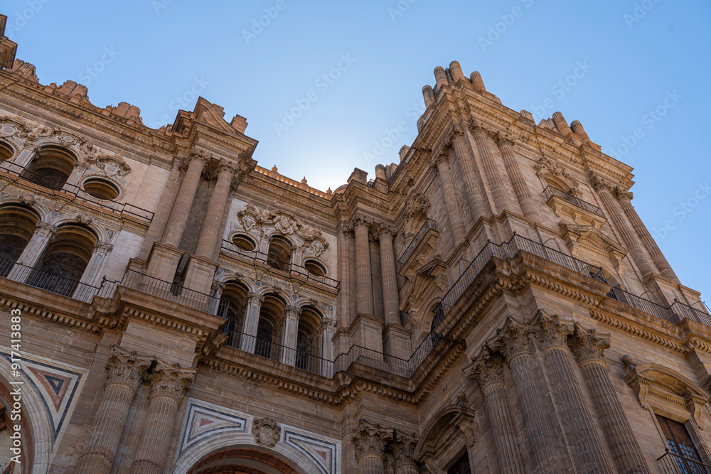 Obraz premium A striking view of the intricate facade of Málaga Cathedral, showcasing its grand architecture against a clear blue sky. Ideal for themes of historic landmarks, architecture, and Spanish heritage.