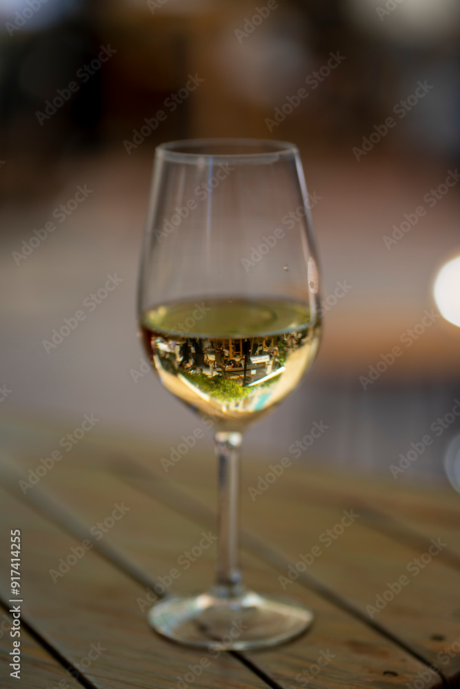 A close-up shot of a white wine glass on a wooden table, capturing the reflection of an outdoor setting. Perfect for themes of leisure, dining, and elegant lifestyle A close-up shot of a white wine glass on a wooden table, capturing the reflection of an outdoor setting. Perfect for themes of leisure, dining, and elegant lifestyle