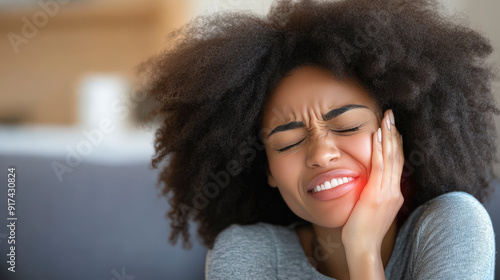 A person with curly hair winces in pain, holding their cheek, possibly indicating a toothache or facial discomfort. photo