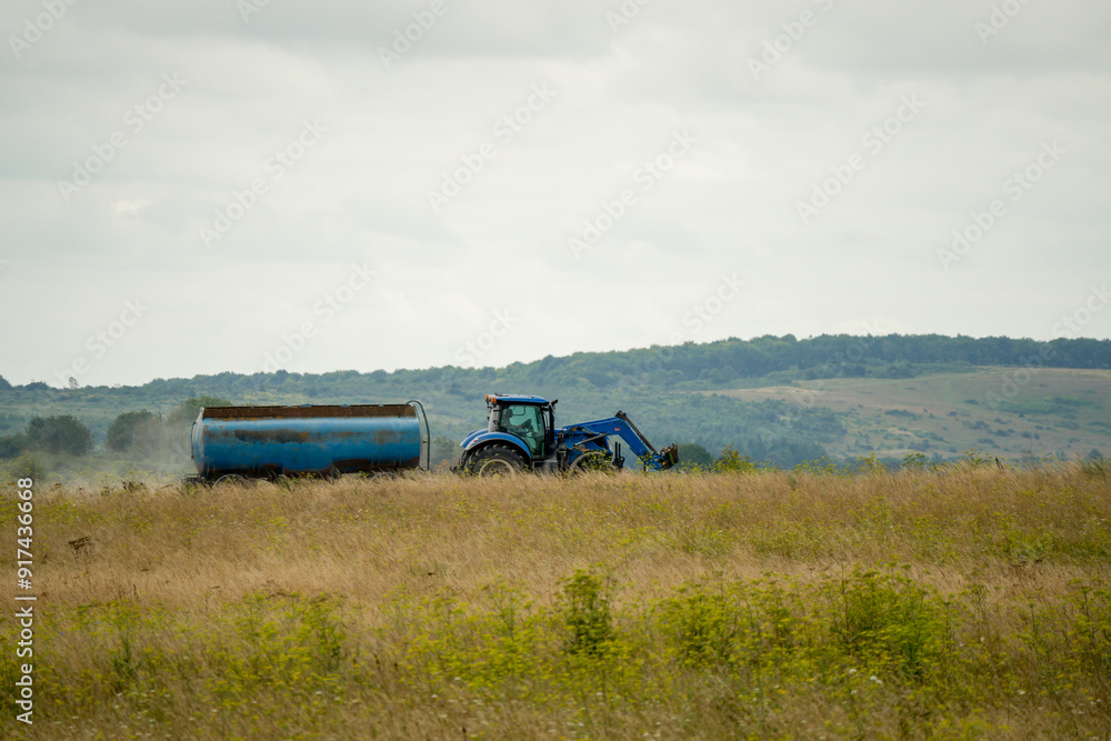 Fototapeta premium large blue New Hollnad T5 tractor towing a 30,000 litre water tanker in countryside