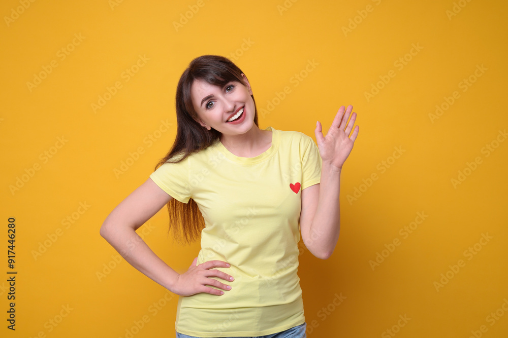 Happy young woman waving on orange background Happy young woman waving on orange background