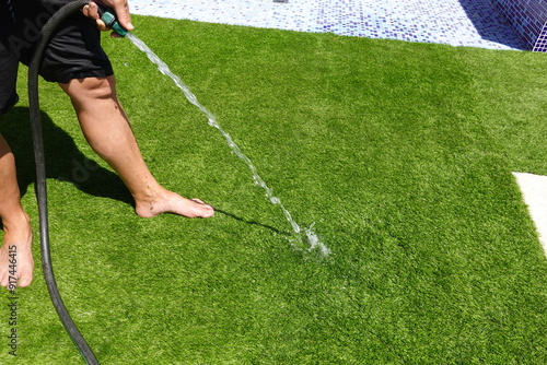 man hoses down artificial grass so it doesn't burn his feet