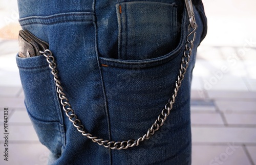 Seitenansicht von schlankem stehenden Mann mit blauer Jeanshose, silberner Gürtelkette und brauner Geldbörse aus Leder in Hosentasche bei Sonne am Nachmittag im Sommer in Stadt