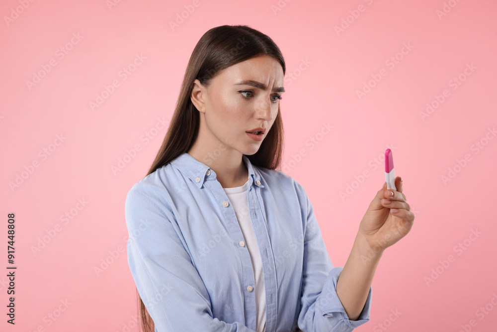 Confused woman holding pregnancy test on pink background Confused woman holding pregnancy test on pink background