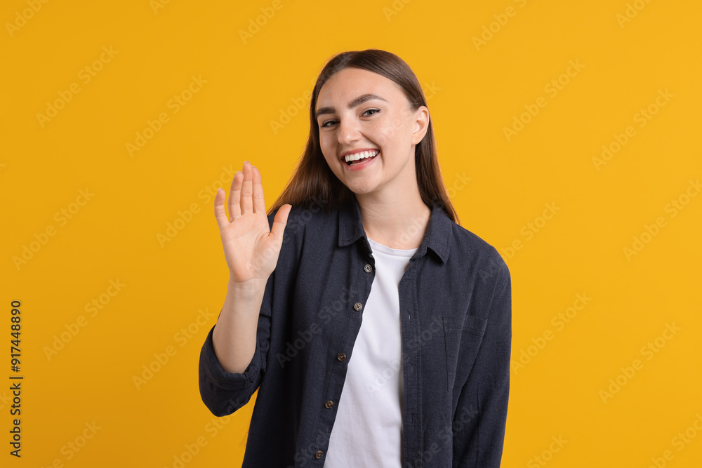 Happy young woman waving on orange background Happy young woman waving on orange background