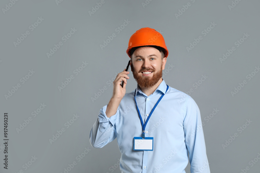 Engineer in hard hat talking on smartphone against grey background Engineer in hard hat talking on smartphone against grey background