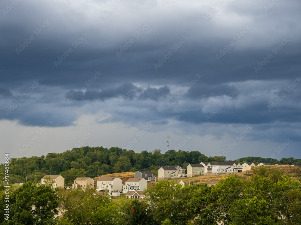 Dramatic thunderstorm clouds hanging over a US residential neighborhood with bright gap in the sky on a summer evening. Dramatic thunderstorm clouds hanging over a US residential neighborhood with bright gap in the sky on a summer evening.