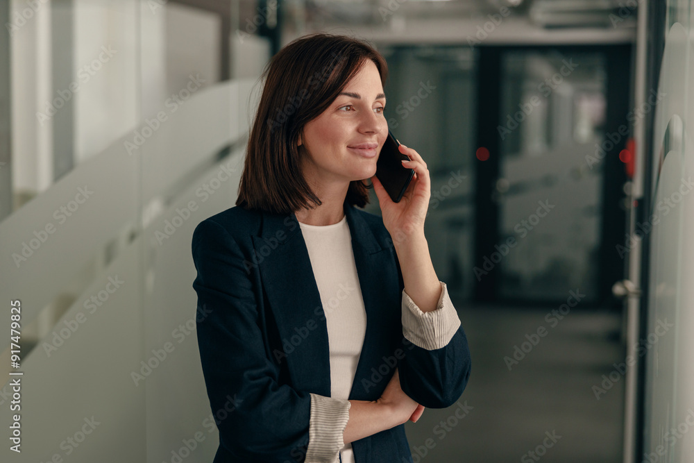 A successful businesswoman is having a phone conversation in a modern office corridor A successful businesswoman is having a phone conversation in a modern office corridor