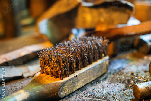 A close-up view of a metalworking workshop featuring a wire brush on a workbench surrounded by tools and materials in a rustic setting