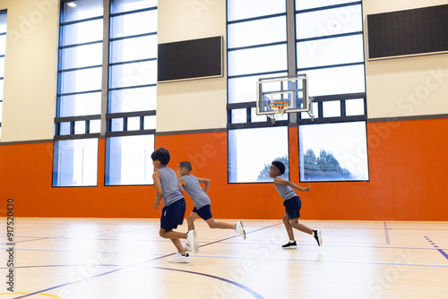 Playing basketball, three boys running in school gymnasium during practice, copy space