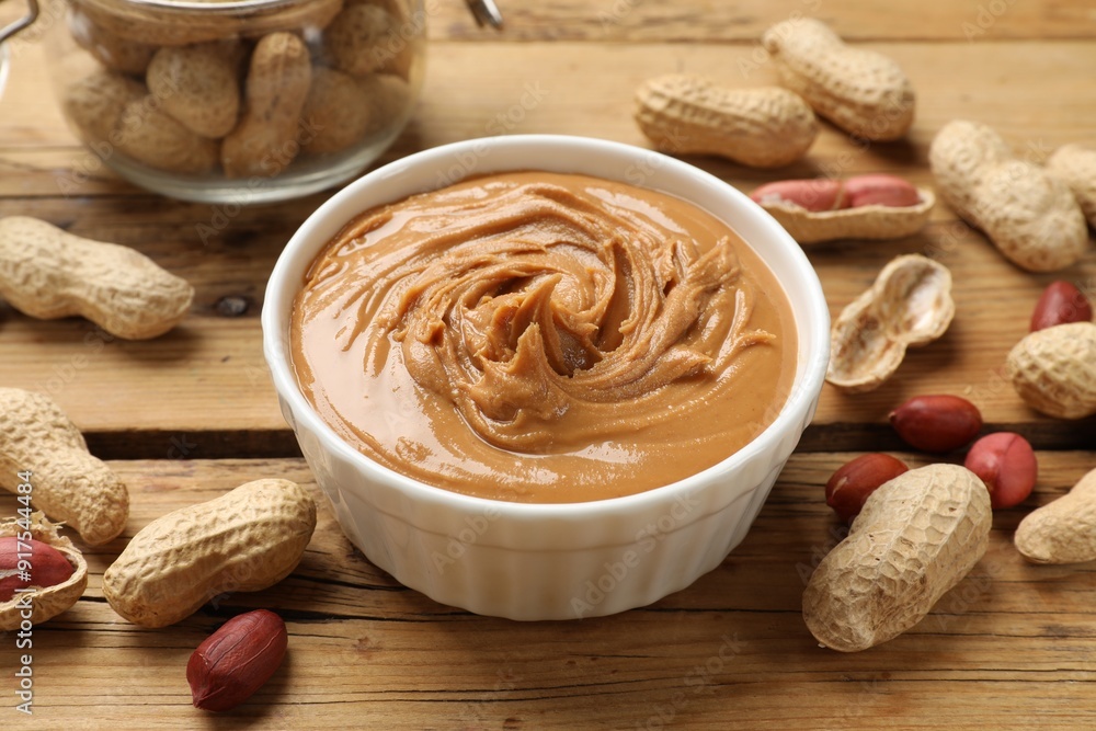 Tasty peanut butter in bowl and groundnuts on wooden table Tasty peanut butter in bowl and groundnuts on wooden table