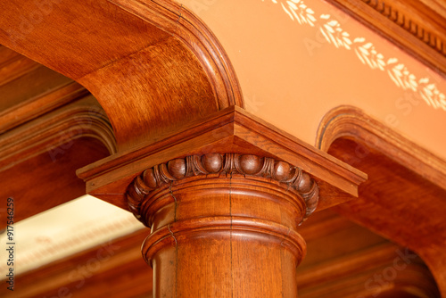 A cherry wood classical load-bearing pilaster. The top of the round pillar has a square carved and decorative molding. The opening is arched with a peach colored paint on the interior stenciled wall. photo