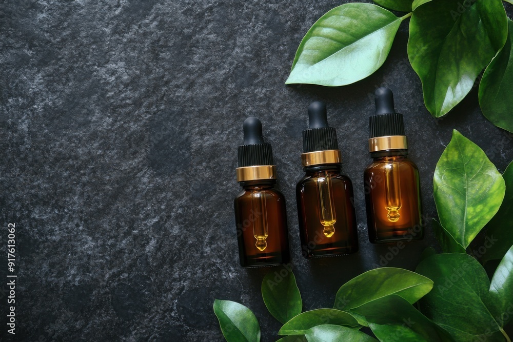 Amber dropper bottles with green leaves on dark stone Amber dropper bottles with green leaves on dark stone