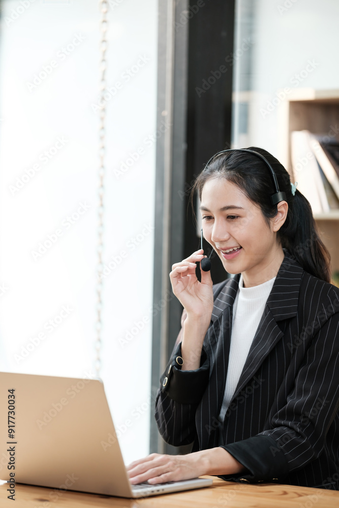 A woman is talking on a phone while sitting at a desk with a laptop