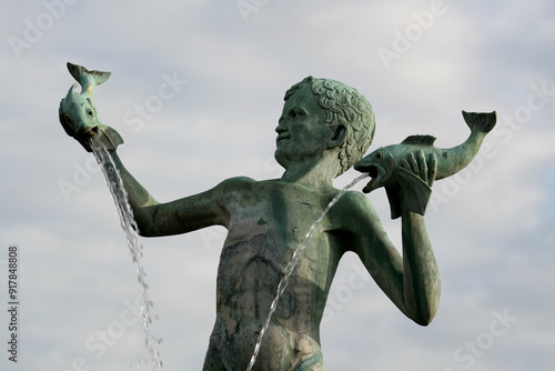 Bronze statue of a young boy holding fish with sea lions around the base of the fountain, St Michaels Fountain Square, Braintree, Essex, England