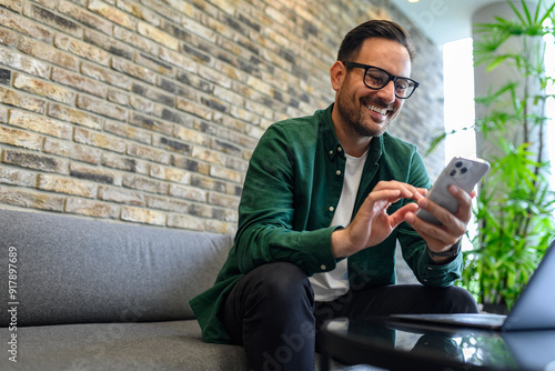 Low angle view of handsome manager checking social media apps over mobile phone on sofa in office