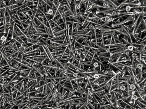 a background of many black screws for construction lies ,equipment for the builder and a screwdriver used to fasten the boards