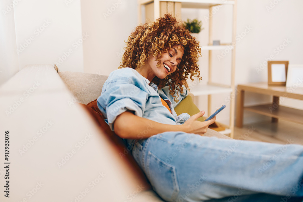 © SHOTPRIME STUDIO - Happy woman holding smartphone and relaxing on cozy couch at home, enjoying online games and chatting in cyberspace © SHOTPRIME STUDIO - Happy woman holding smartphone and relaxing on cozy couch at home, enjoying online games and chatting in cyberspace