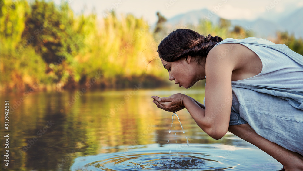 Fototapeta premium Young woman drinks water from the river