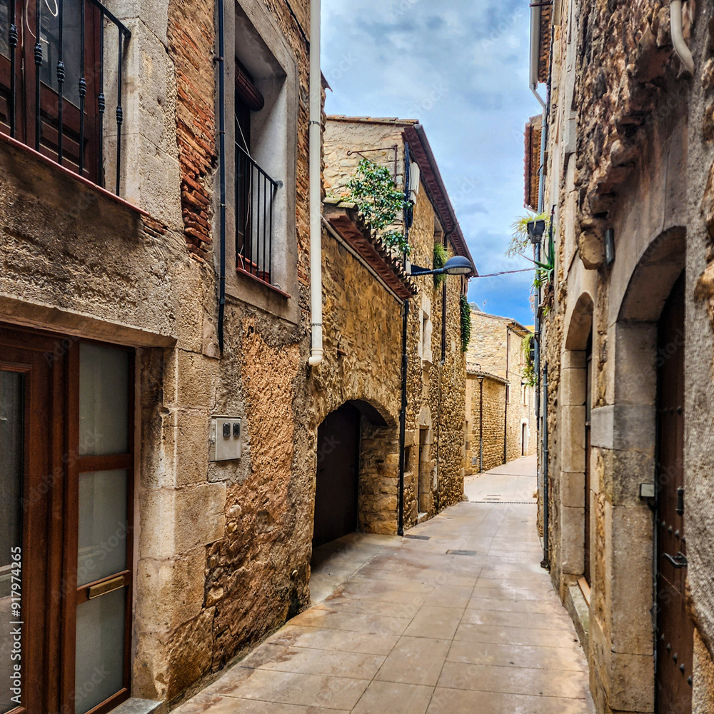 Fototapeta premium Narrow streets of the old town. Old stonework on facades with gates and balconies. Cityscape. Celra. Catalonia. Spain.