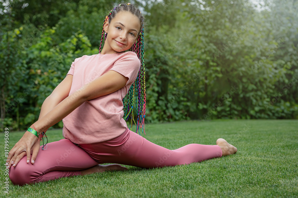 Flexible smiling young girl is performing gymnastic exercises in the garden. Horizontally. Flexible smiling young girl is performing gymnastic exercises in the garden. Horizontally.
