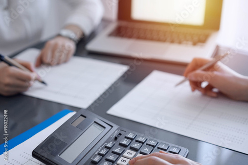 Two accountants use a calculator and laptop computer for counting taxes or revenue balance. Business, audit, and taxes concepts photo