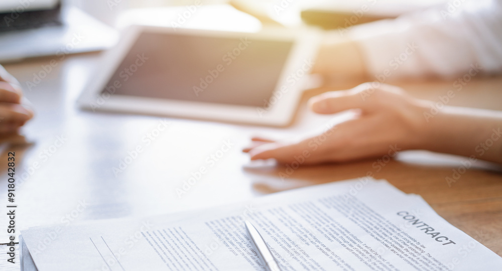 Contract papers are lying at the wooden desk while business people discussing something at the wooden desk at the background. Teamwork, partnership, contract signing concept Contract papers are lying at the wooden desk while business people discussing something at the wooden desk at the background. Teamwork, partnership, contract signing concept