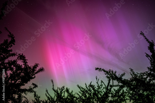 The aurora borealis creates a magical scene in the summer sky, its vivid colors reflecting off a calm lake in Germany, offering a unique and unforgettable sight.