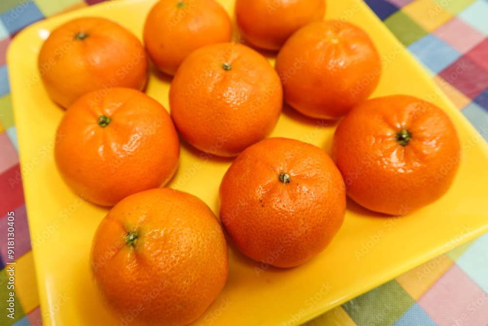 close up top shot of nine orange citrus tangerine fruit on a yellow plate on a table with colourful table cloth close up top shot of nine orange citrus tangerine fruit on a yellow plate on a table with colourful table cloth