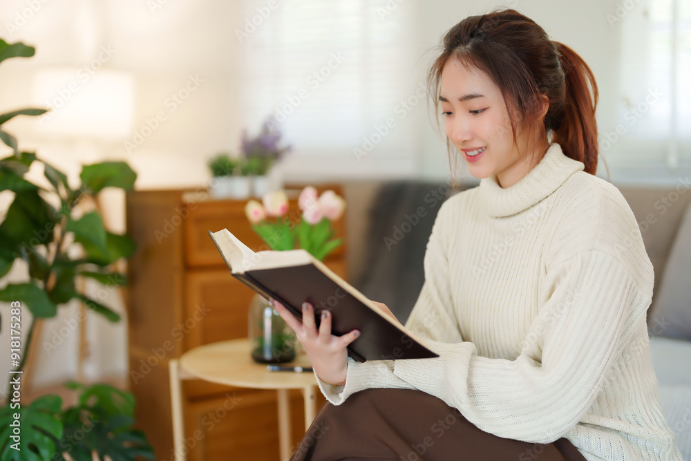 Young asian women in sweater reading a book and learning about literature story with enjoying while sitting on couch to relaxation and doing activity to spending time with slow life lifestyle at home Young asian women in sweater reading a book and learning about literature story with enjoying while sitting on couch to relaxation and doing activity to spending time with slow life lifestyle at home