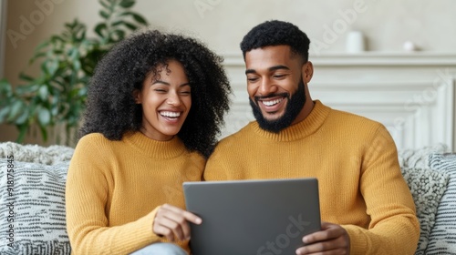 Couple shopping online for Black Friday deals, sitting together on a sofa, laughing and pointing at the laptop screen 