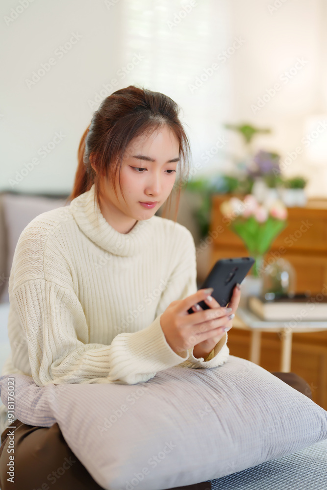Young asian women in sweater enjoying with surfing entertainment on smartphone while sitting on comfortable couch to relaxation and doing activity for spending time with slow life lifestyle at home Young asian women in sweater enjoying with surfing entertainment on smartphone while sitting on comfortable couch to relaxation and doing activity for spending time with slow life lifestyle at home