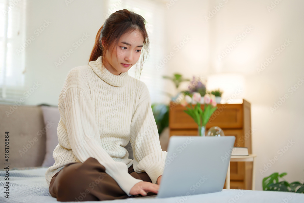 Young asian women in sweater sitting on the couch and using laptop to enjoying with chatting on social media while relaxation and doing activity to spending time with slow life lifestyle at home Young asian women in sweater sitting on the couch and using laptop to enjoying with chatting on social media while relaxation and doing activity to spending time with slow life lifestyle at home