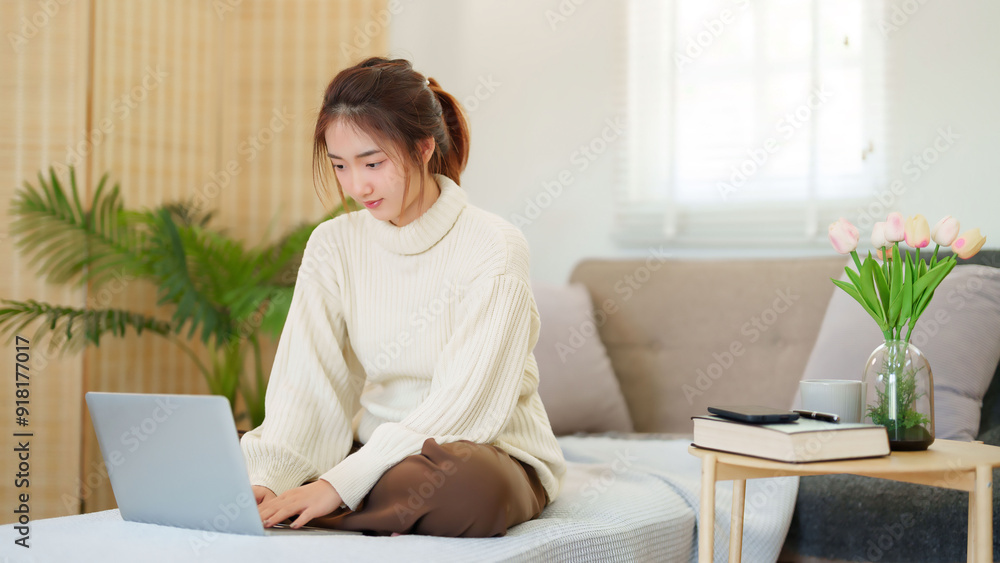 Young asian women in sweater sitting on the couch to enjoying with surfing social media entertainment on laptop while relaxation and doing activity to spending time with slow life lifestyle at home Young asian women in sweater sitting on the couch to enjoying with surfing social media entertainment on laptop while relaxation and doing activity to spending time with slow life lifestyle at home
