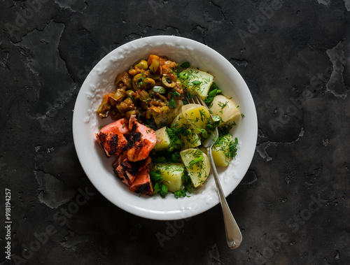 Simple outdoor food - boiled potatoes with herbs, grilled salmon, caponata on a dark background, top view photo