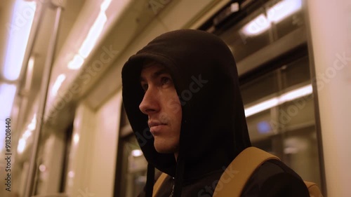 Close-up of unfriendly suspicious black hooded young man look around in a moving subway car 4K