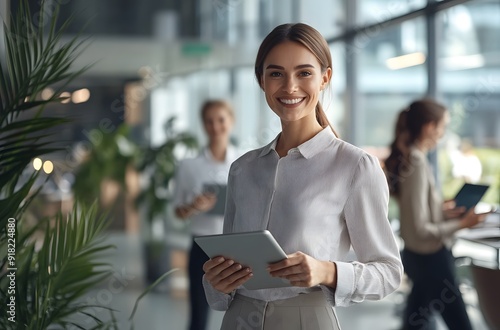 A smiling businesswoman stands in an office holding her tablet