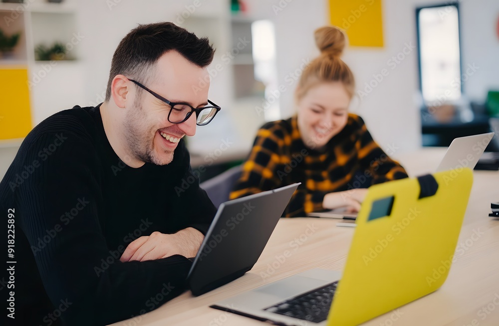 A smiling man and woman sitting at an office desk, using laptops A smiling man and woman sitting at an office desk, using laptops