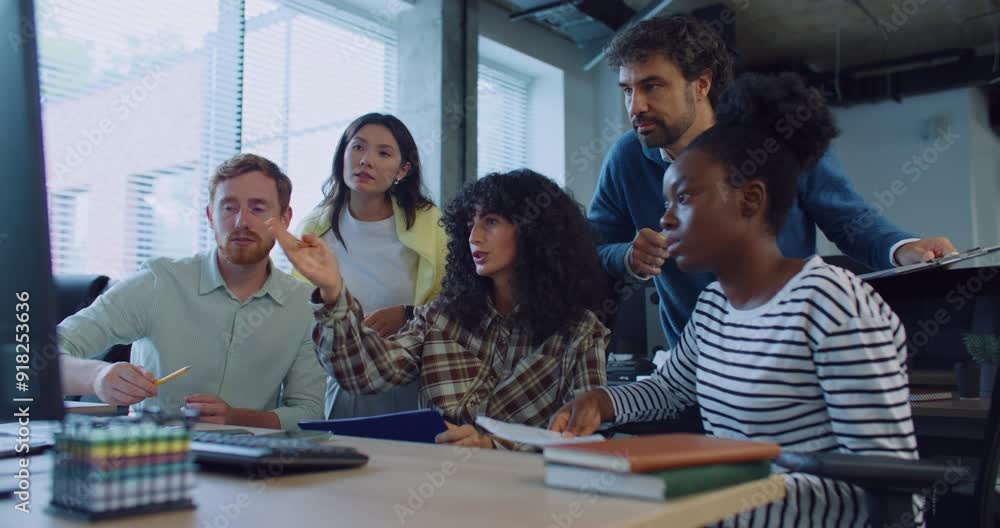 Group of multi-ethnic colleagues gathering together in front of one monitor. Woman in middle with curly hair confused about something. People pointing at screen. Team meeting. Finding solution. Group of multi-ethnic colleagues gathering together in front of one monitor. Woman in middle with curly hair confused about something. People pointing at screen. Team meeting. Finding solution.
