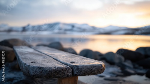 A frosty wooden bench by a peaceful lakeside at sunrise, with a view of snow-covered mountains in the background, creating a tranquil and serene setting. photo