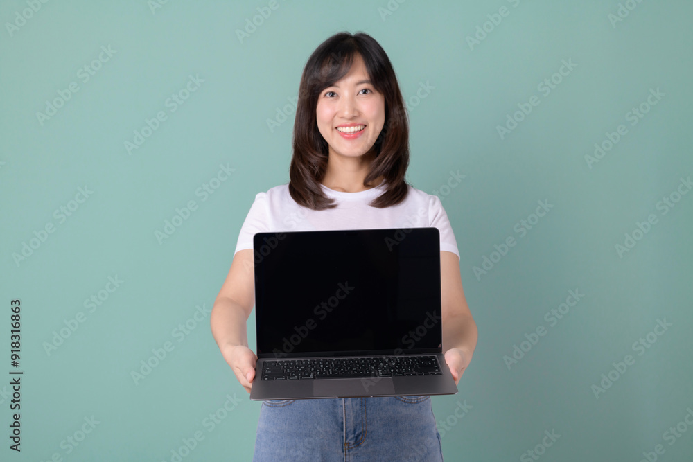 Technology advertisement. cheerful beautiful Asian woman in white t-shirt and holding laptop mockup of blank screen on green background. Technology advertisement. cheerful beautiful Asian woman in white t-shirt and holding laptop mockup of blank screen on green background.
