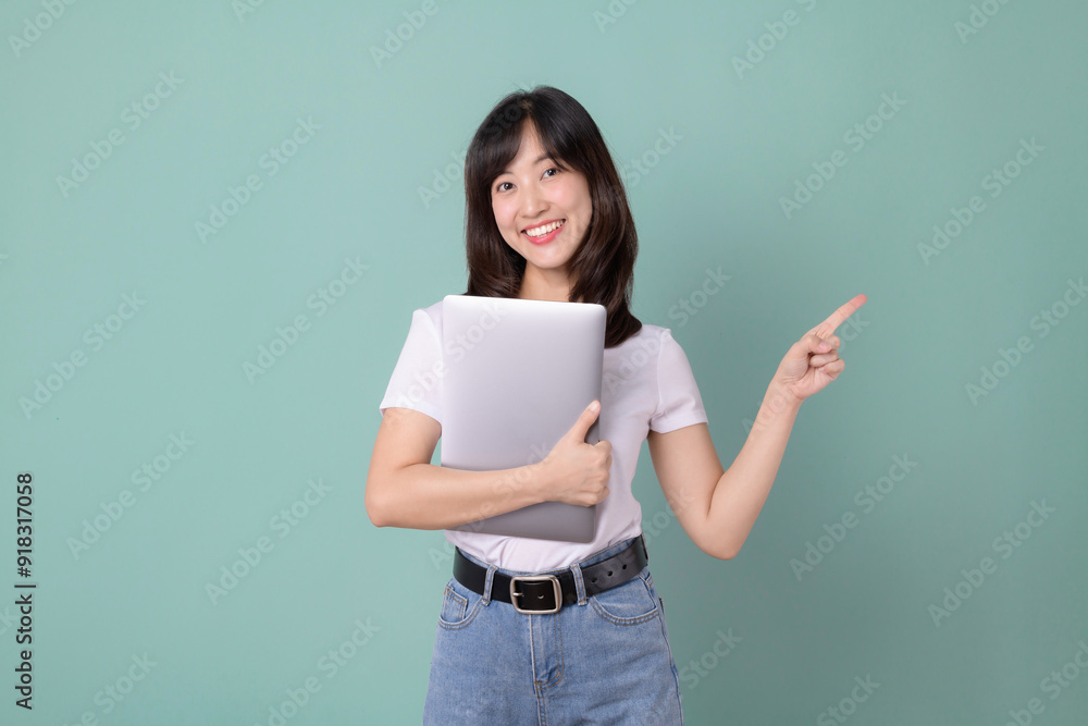 Technology lover. Cheerful asian woman hugging laptop while pointing finger to free empty copy space. Casual female hug laptop isolated on green background. Back to school concept for advertisement. Technology lover. Cheerful asian woman hugging laptop while pointing finger to free empty copy space. Casual female hug laptop isolated on green background. Back to school concept for advertisement.