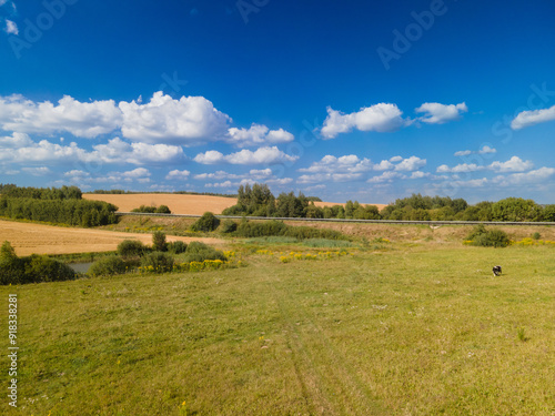 Landscape view from drone, yellow and green fields and haystacks, sky with white clouds. 