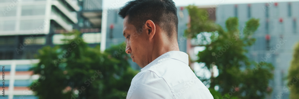 Young businessman is walking down the street and looking at a smartphone on modern building background, panorama Young businessman is walking down the street and looking at a smartphone on modern building background, panorama