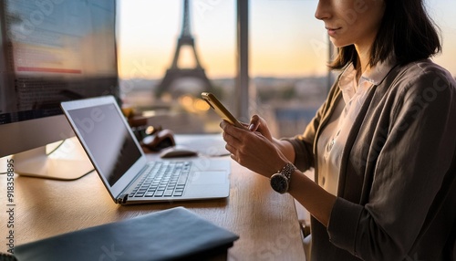 Side view of crop focused woman with dark hair messaging on cellphone while sitting with desktop computer in office in Paris