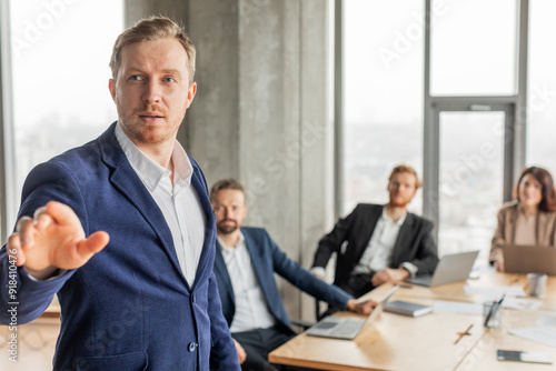 Wallpaper Mural A man in a blue suit stands in front of a conference table and presents to a group of colleagues. The colleagues are sitting at the table, listening attentively. Torontodigital.ca