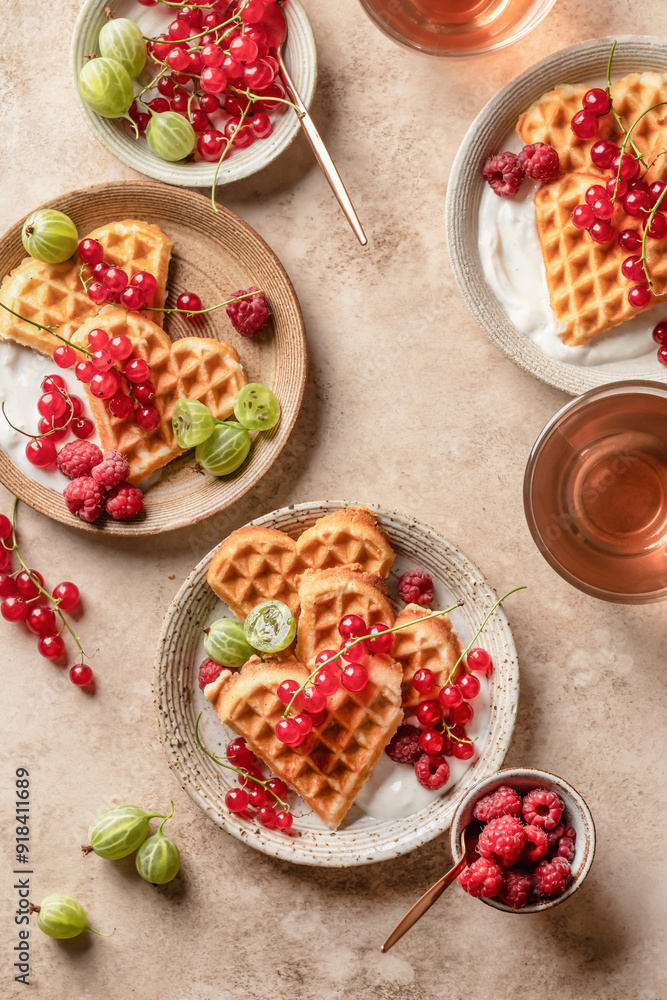 Homemade waffles with summer berries and yogurt served for sweet breakfast with tea on beige background. Heart shaped waffles top view Homemade waffles with summer berries and yogurt served for sweet breakfast with tea on beige background. Heart shaped waffles top view