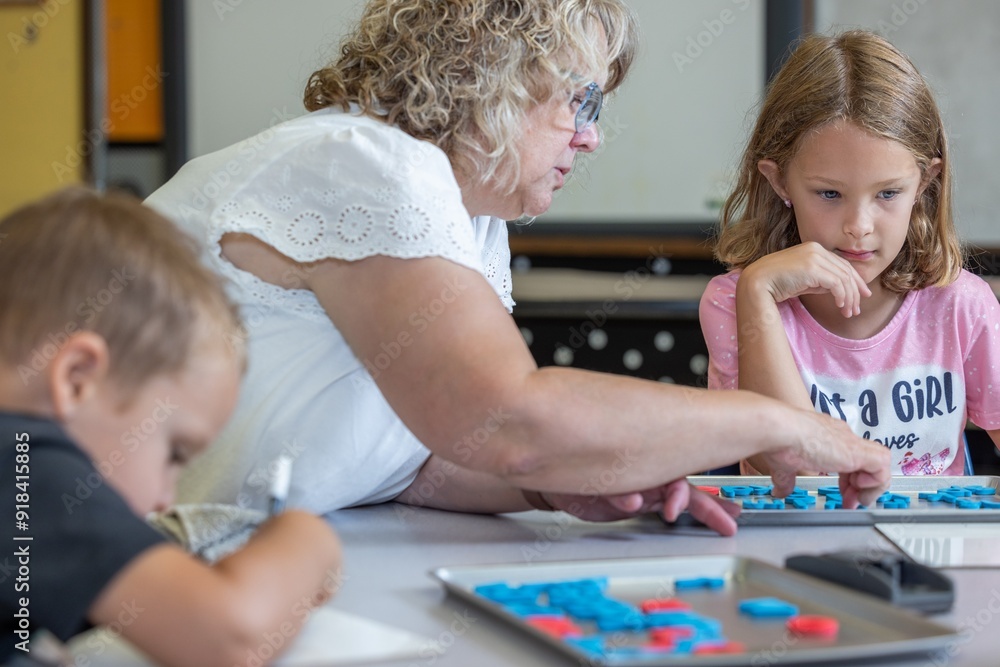 A teacher is helping a young girl with a spelling. The teacher is pointing to a letter, and the girl is looking at it intently. A teacher is helping a young girl with a spelling. The teacher is pointing to a letter, and the girl is looking at it intently.