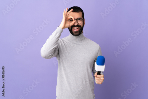 Adult reporter man with beard holding a microphone over isolated purple background showing ok sign with fingers